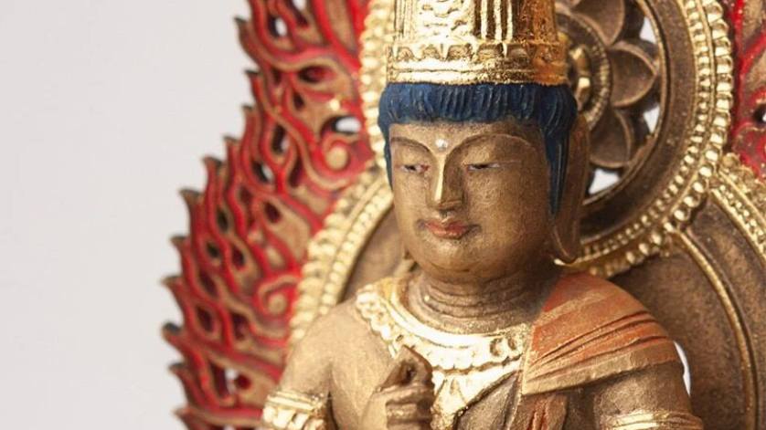 Close-up of a painted Buddhist statue with a calm expression, ornate golden crown, and red flame halo in the background.