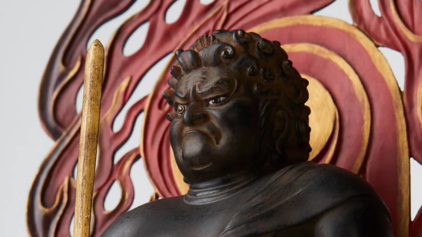 Close-up of a dark Fudo Myoo statue with a red and gold flame halo in the background.