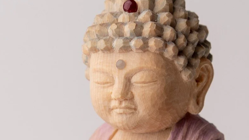 Close-up of a carved wooden Buddha statue with closed eyes and detailed hair ornaments.