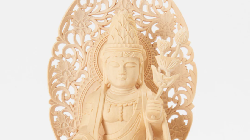 A pale wooden bodhisattva statue holding a lotus flower, with an intricately carved halo behind it.