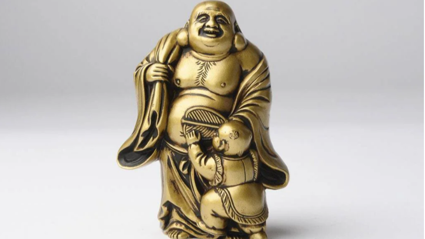A small Hotei statue smiling beside a child holding a fan.