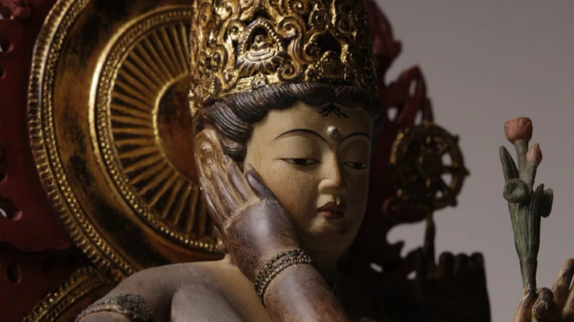 Close-up of a crowned bodhisattva statue holding a lotus flower, with a golden halo in the background.