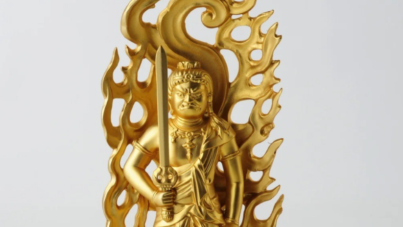 A golden Fudo Myoo statue standing with a sword, framed by a flame-shaped halo.