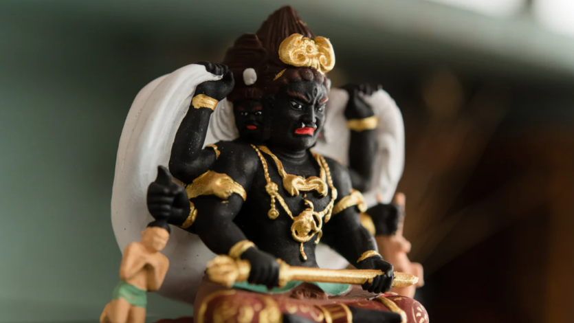 Close-up of a black Buddhist statue with gold ornaments, multiple arms, and white cloth-like decorations.