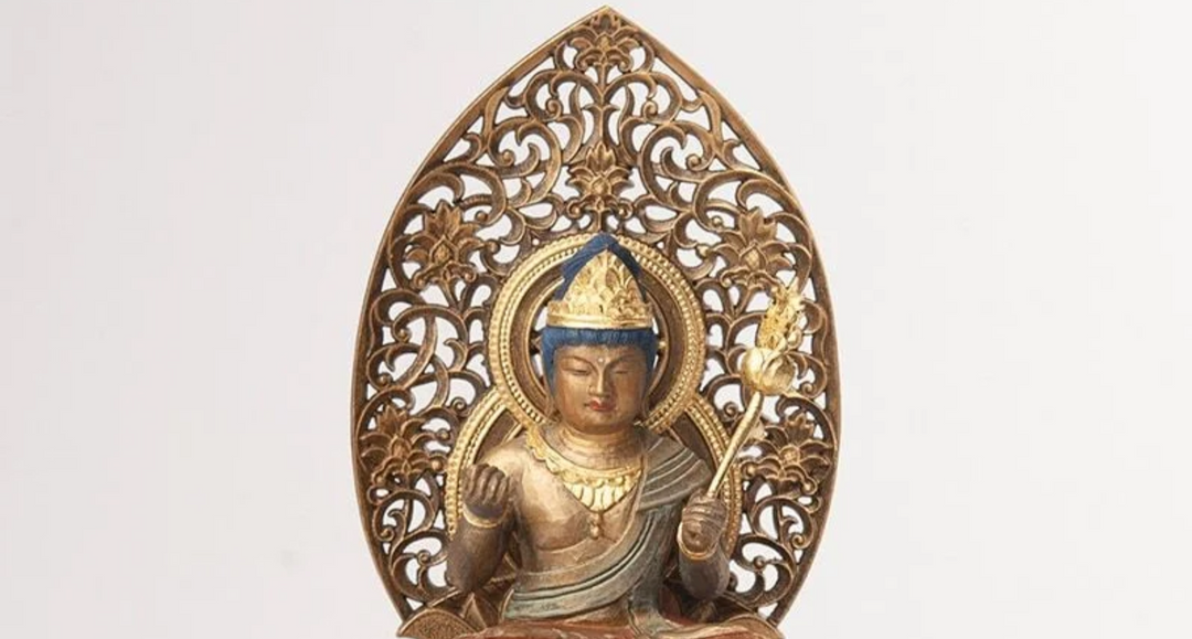 Seated Buddhist statue with an ornate halo, crown, and ritual staff, illustrating the visual features often used to distinguish a Buddha from a bodhisattva.