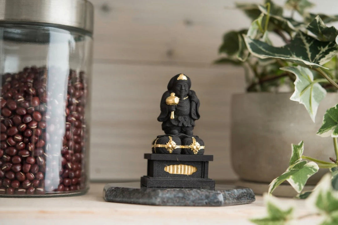 Small Daikokuten statue displayed in a home setting beside plants and household items, illustrating considerations for respectful Buddha statue placement.
