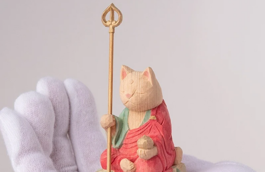 Whimsical wooden Enmei Jizo-inspired cat figurine holding a staff and jewel, representing the life-extending and protective symbolism of Jizo.