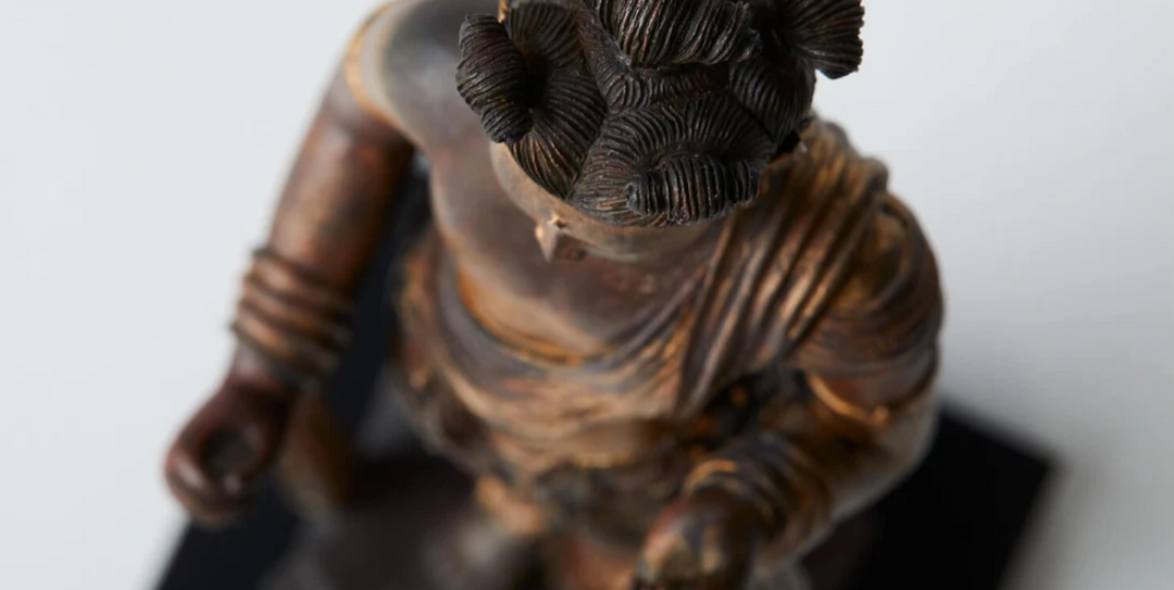 Close-up of a Chinese Buddhist statue with tightly curled hair and flowing robes, highlighting sculptural details that reflect blended Buddhist artistic traditions.