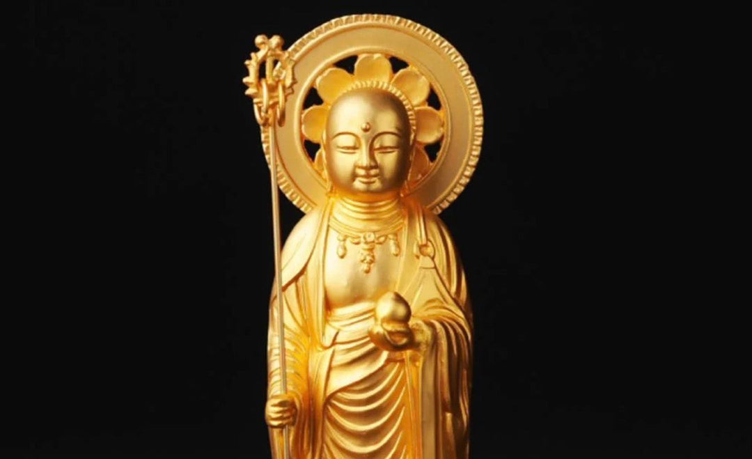Golden Jizo Bosatsu statue holding a staff and sacred jewel, shown against a black background with a radiant halo.