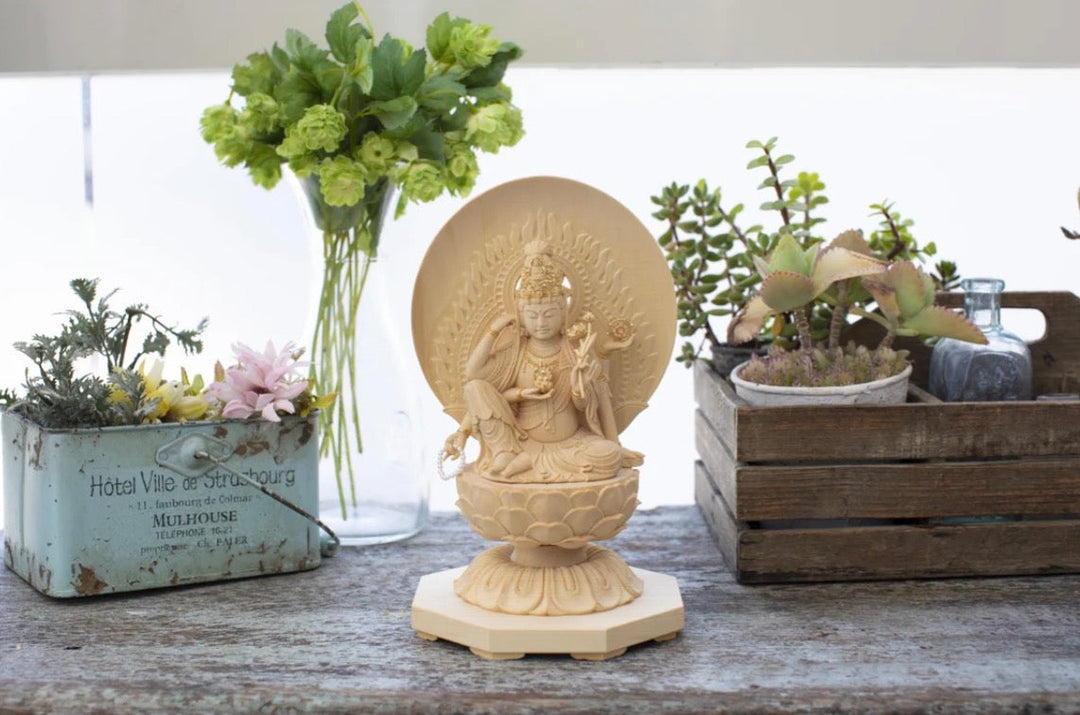 Nyoirin Kannon statue displayed in a peaceful home setting with flowers and plants, representing compassion, prayer, and devotional offerings.
