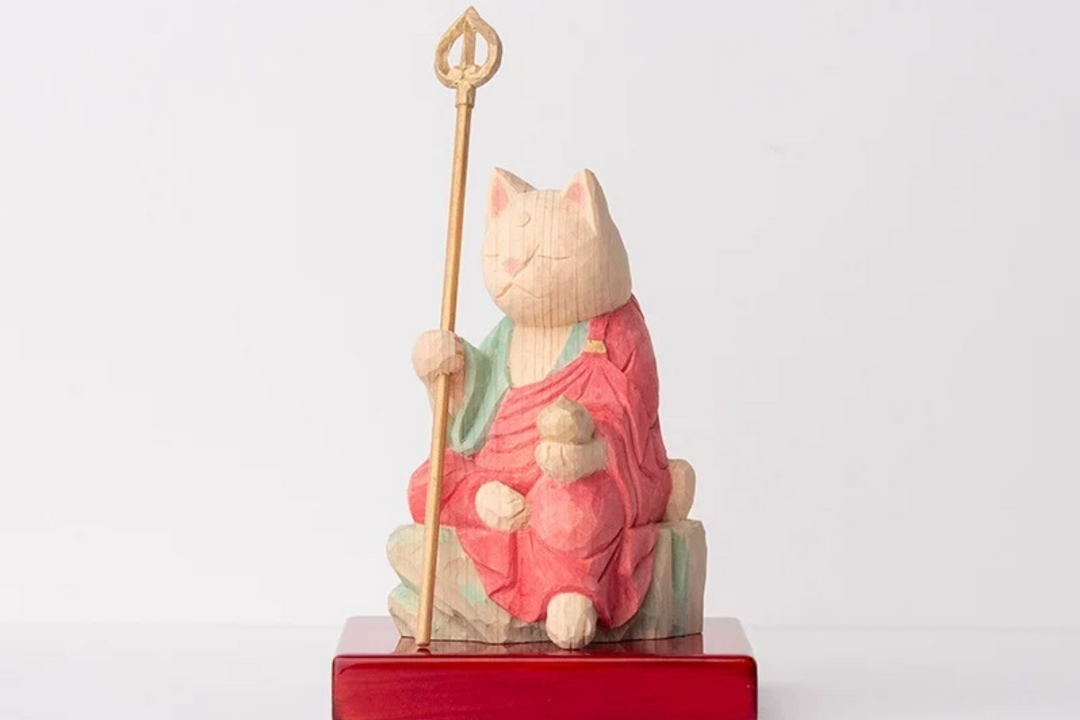 Wooden Jizo-inspired cat figurine holding a staff and wish-fulfilling jewel, illustrating the sacred jewel’s symbolism of blessings, protection, and fulfilled wishes in Buddhist iconography.