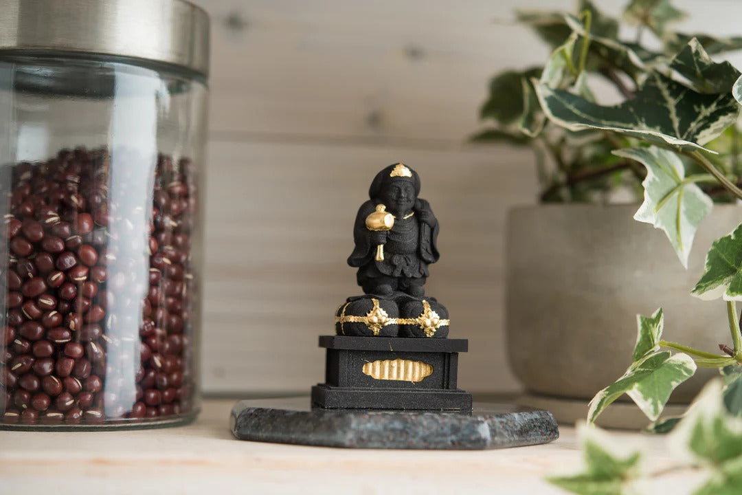 Black wooden Daikokuten statue holding a mallet and treasure sack, seated on a base, displayed on a table