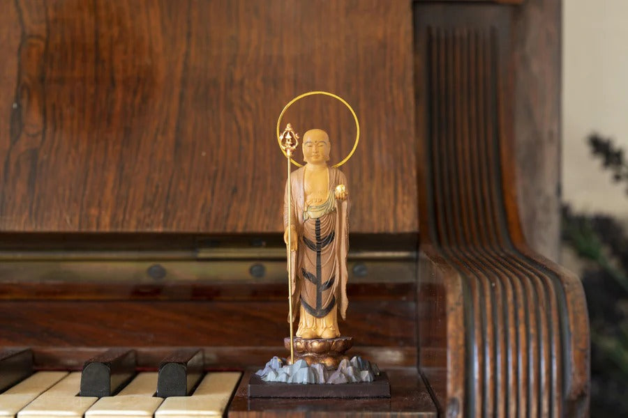 Wooden Jizo Bodhisattva statue standing on a lotus base with a halo and staff, displayed on a vintage piano