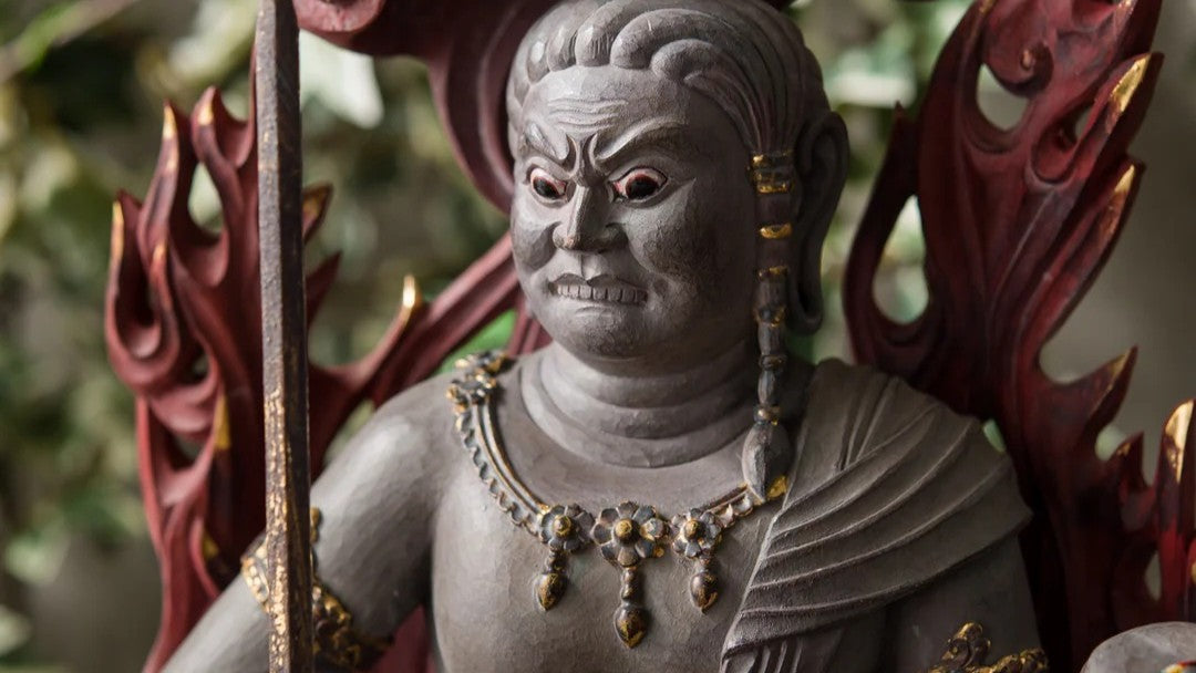 Close-up of a Fudo Myoo (Acala) statue with fierce expression, holding a sword, with a flaming halo