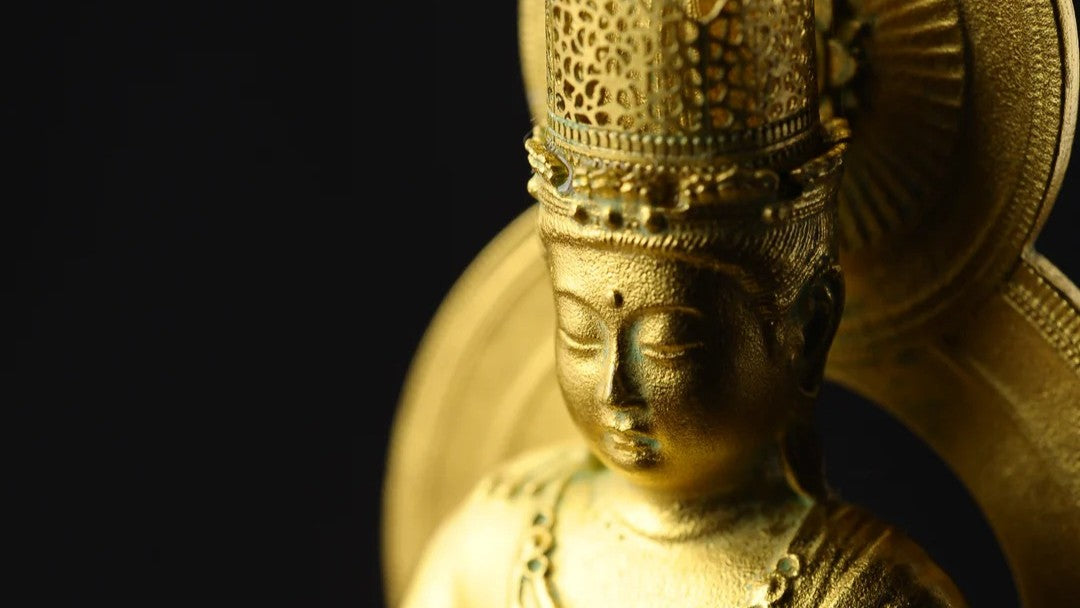 Close-up of a golden Bodhisattva statue with ornate crown and halo against a dark background